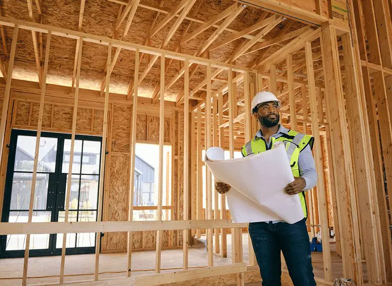 Construction worker holding blueprints inside building frame.